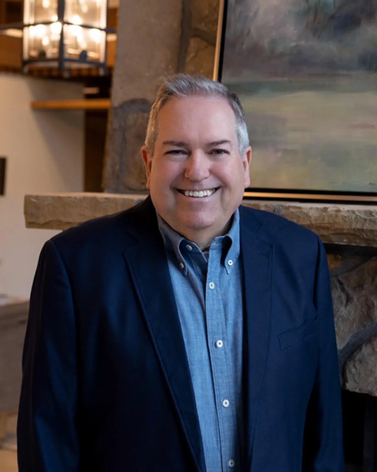 Smiling man in a dark blazer and blue shirt indoors.