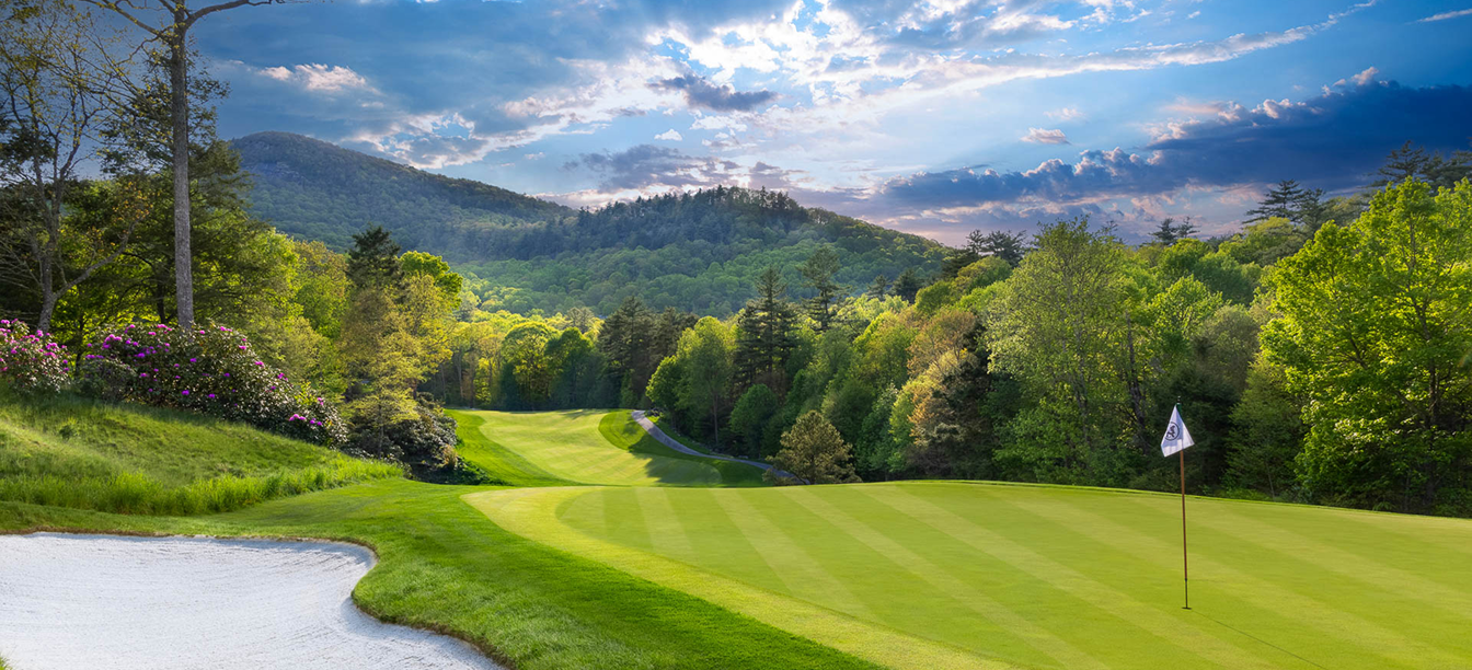 Scenic golf course surrounded by lush green hills under a cloudy sky.