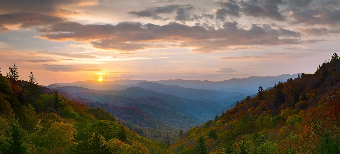 Sunset over rolling mountains with vibrant autumn foliage.