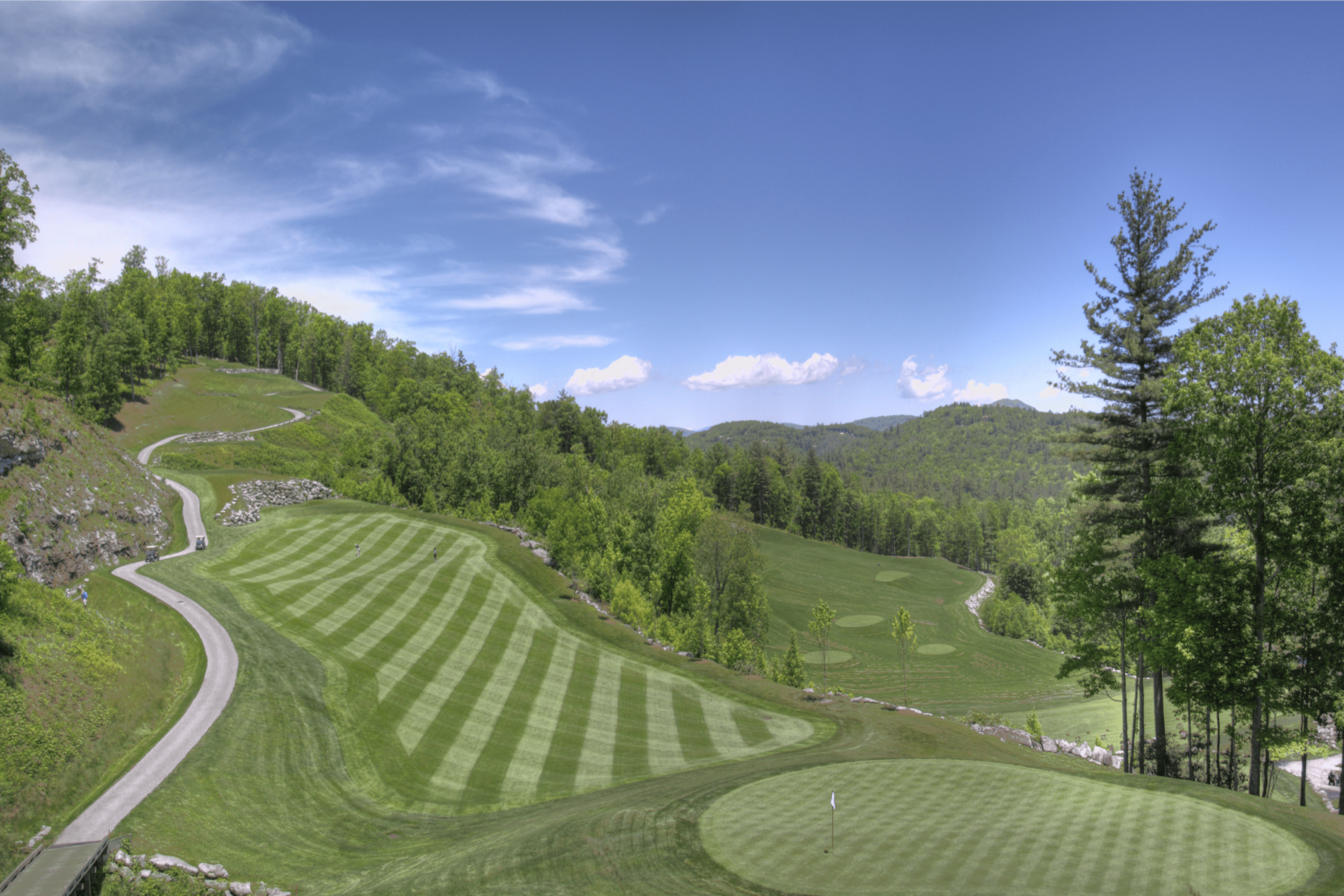 A scenic golf course with striped fairways and surrounding hills.