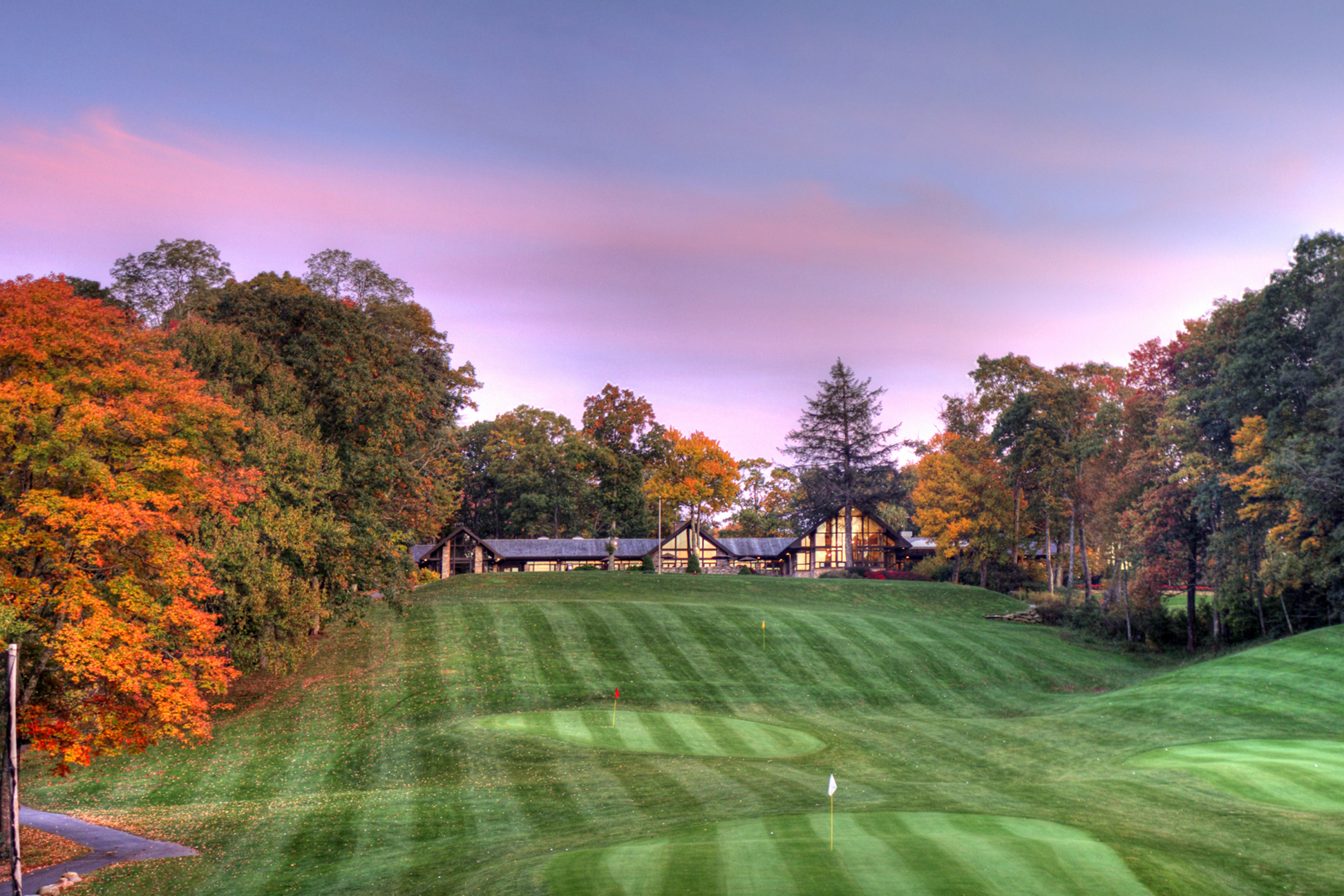A serene golf course at sunset with lush green fairways and trees.