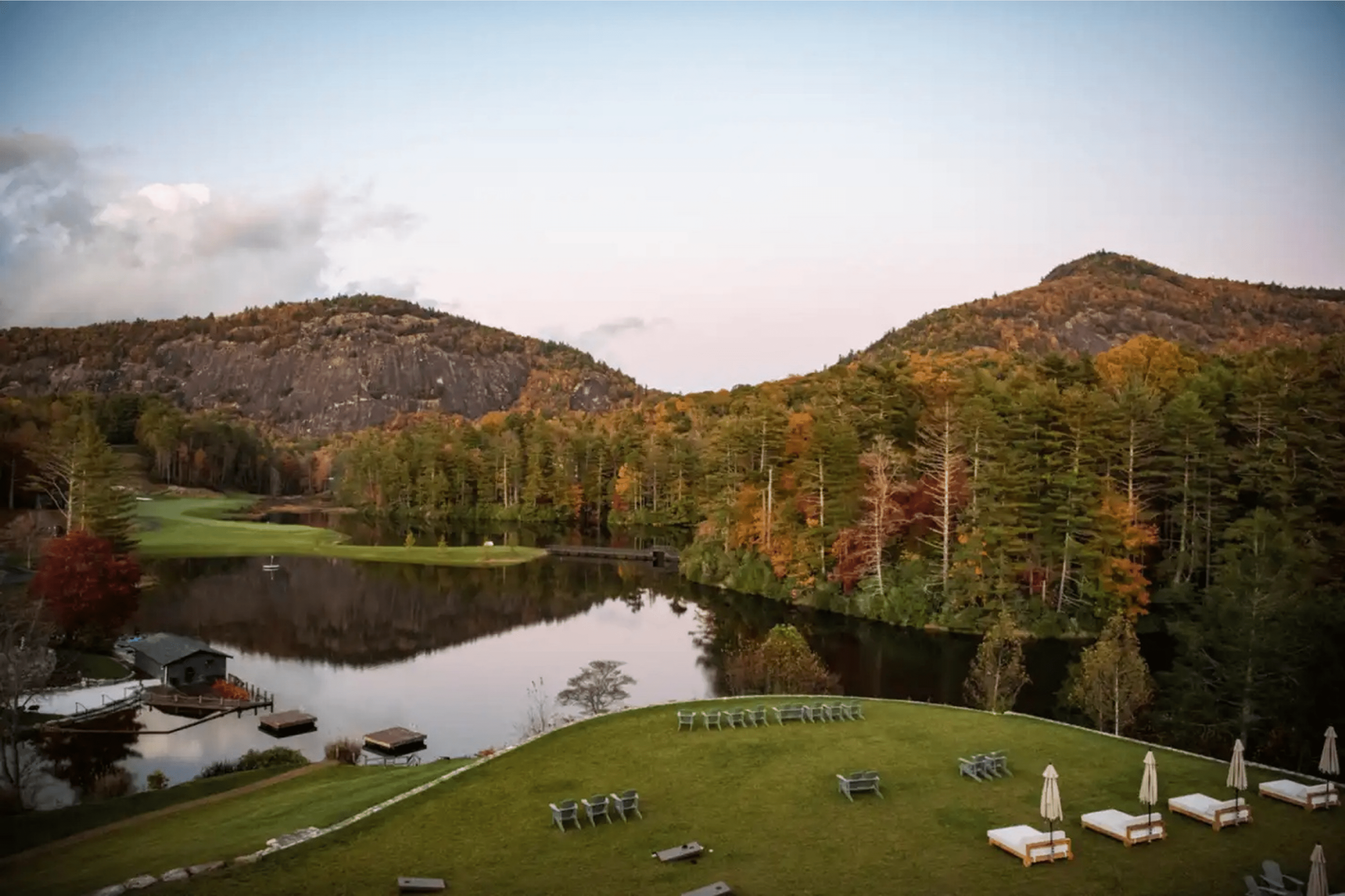 Scenic lakeside view with autumn trees and hills at sunset.