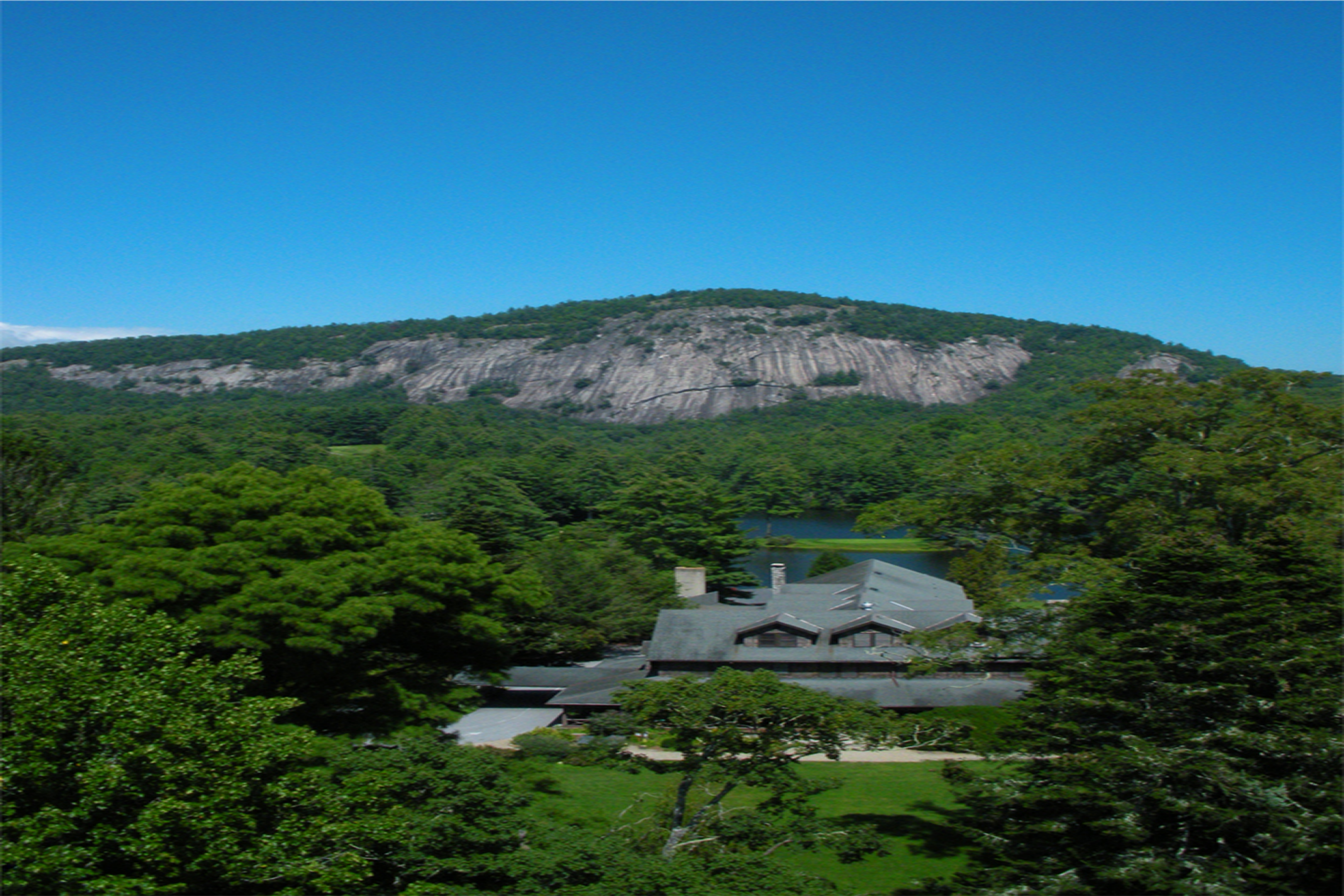 Traditional Japanese building amidst lush greenery and a rocky mountain.
