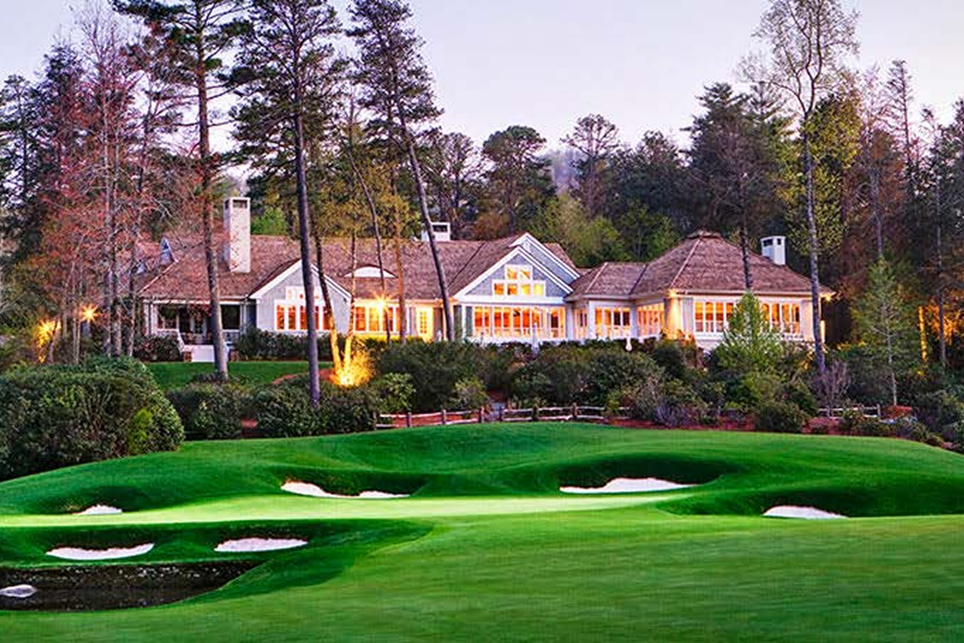 A serene golf course with sand bunkers and a clubhouse at sunset.