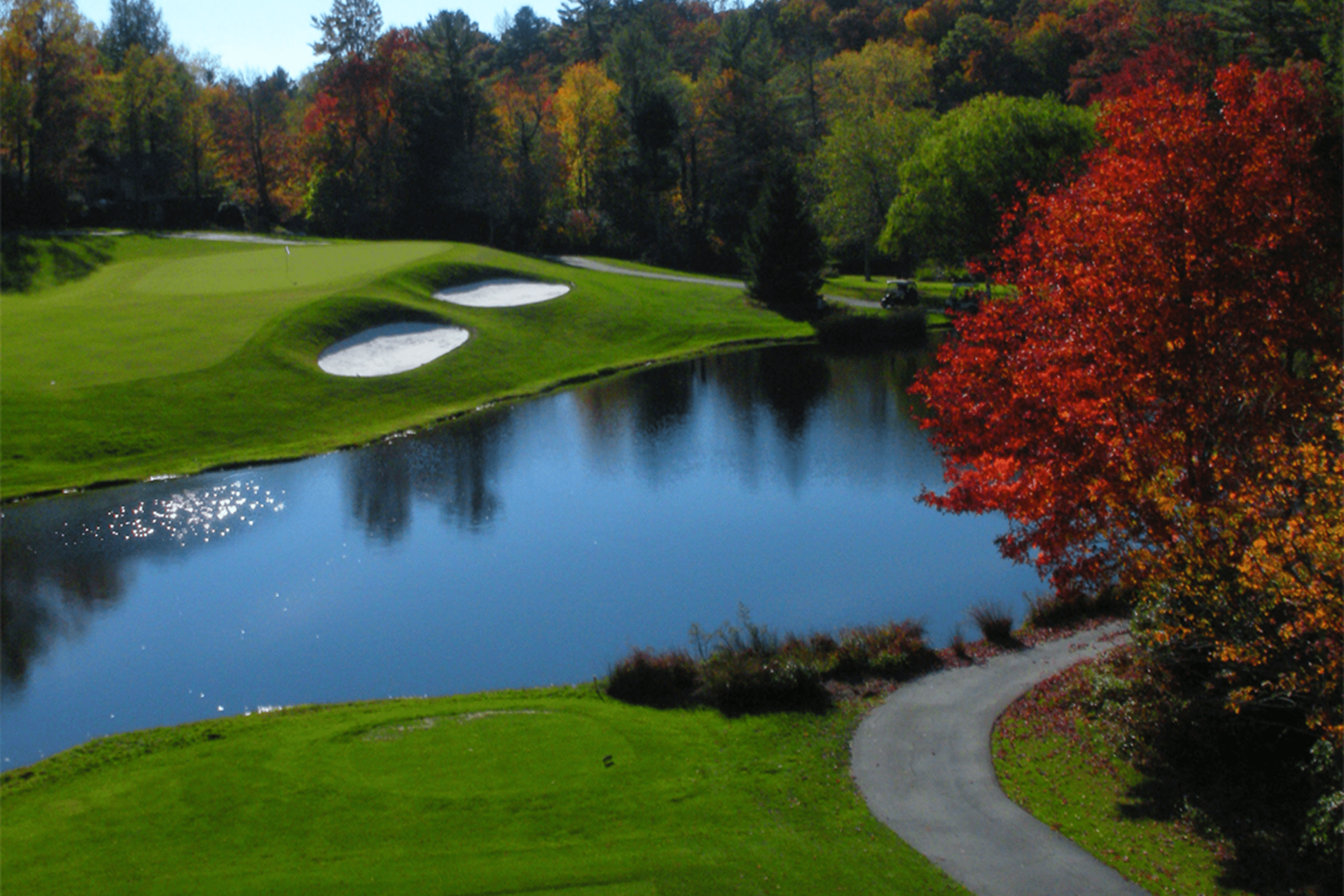 Scenic golf course with water and vibrant autumn trees.