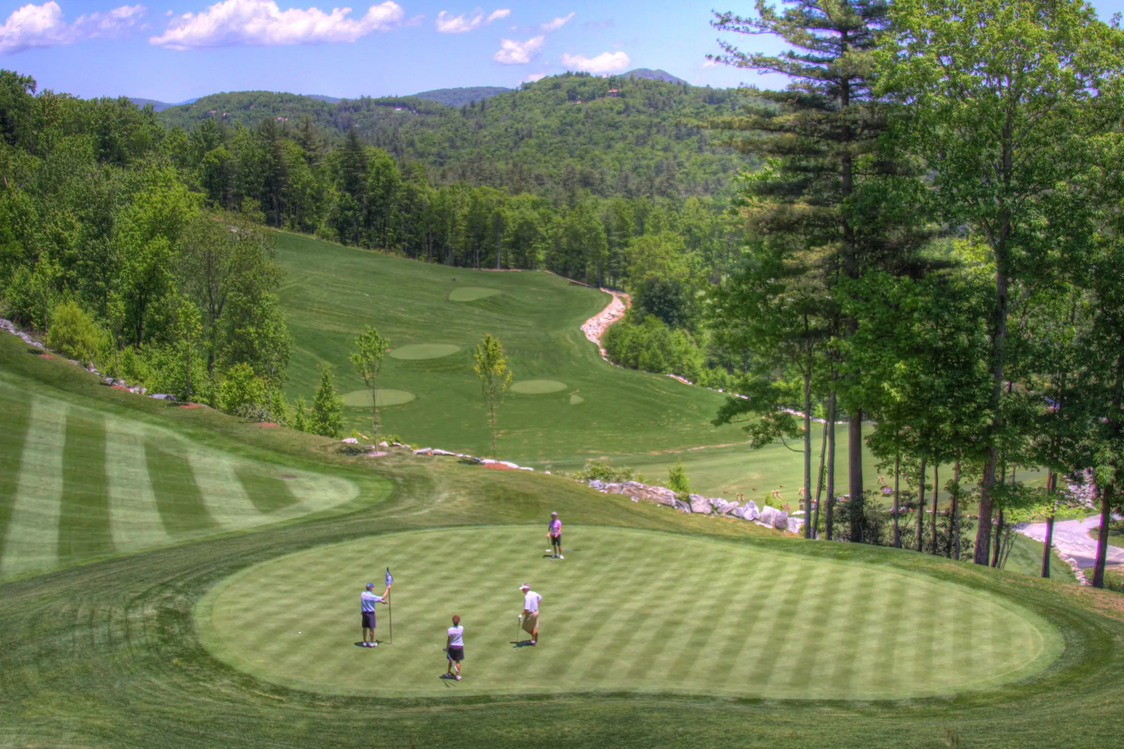 Golfers playing on a lush, green course with rolling hills and trees.