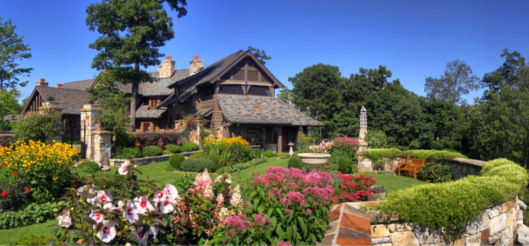 A charming stone house surrounded by a colorful garden under a clear sky.