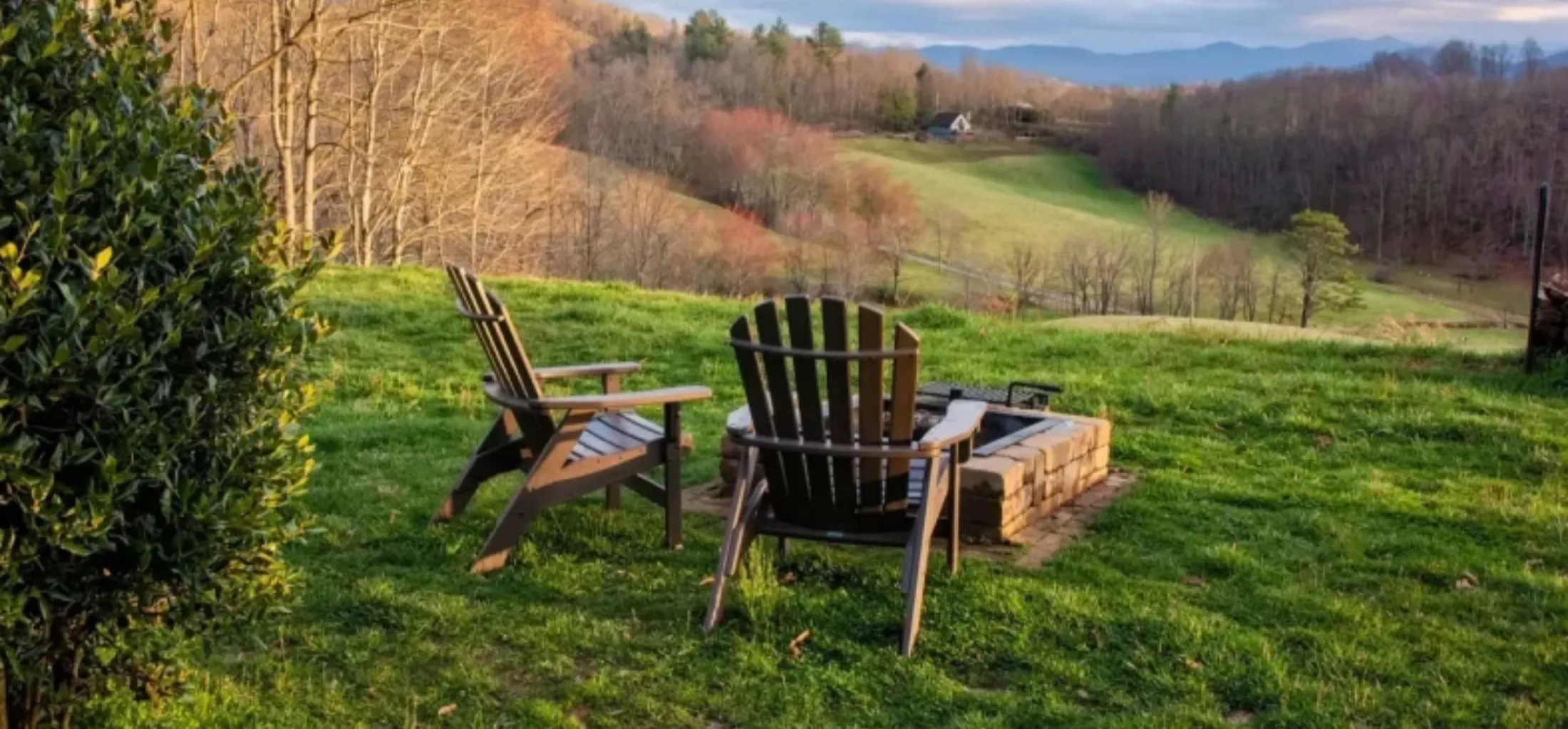 Two wooden chairs around a fire pit overlooking a scenic hillside.