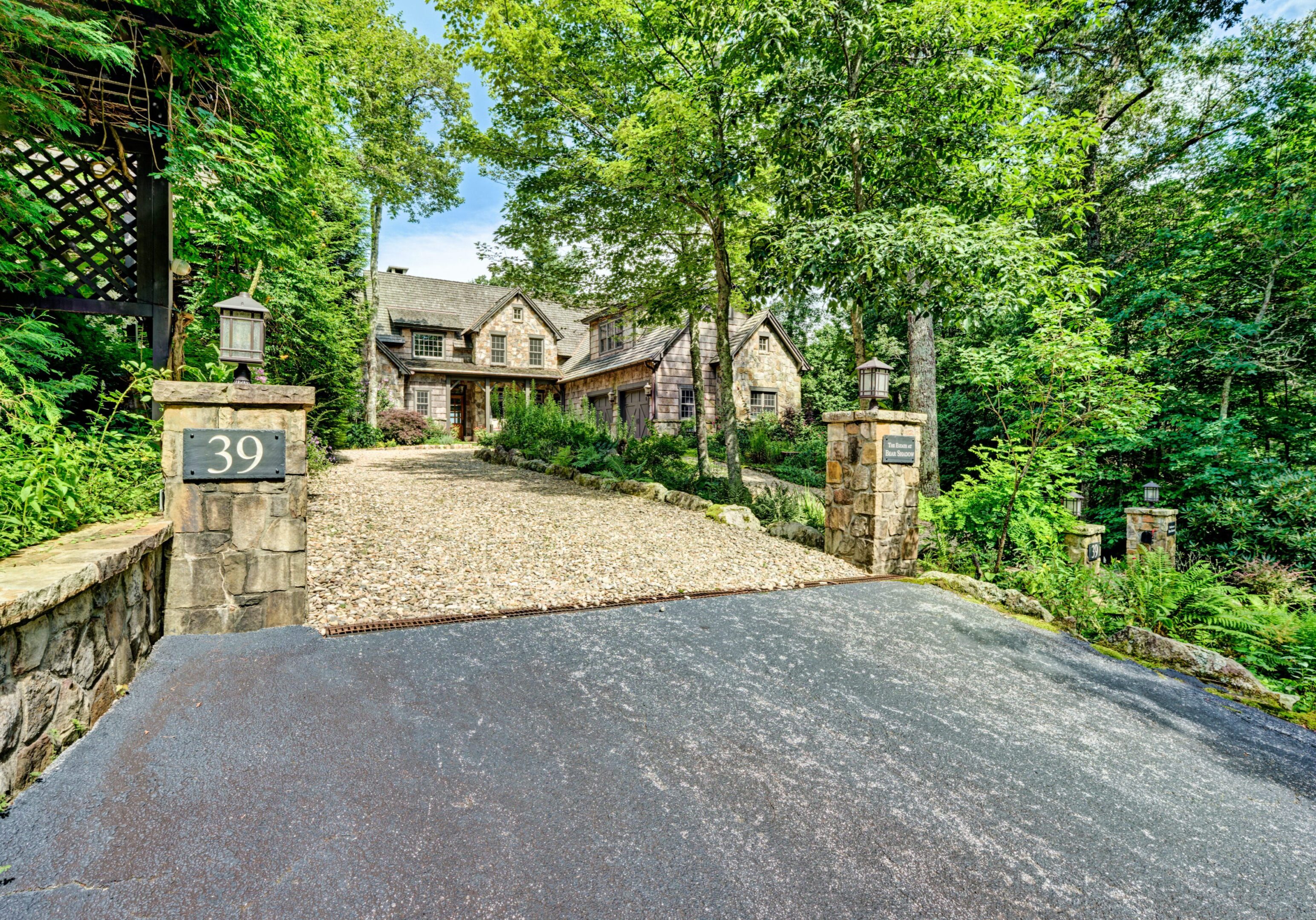 Elegant stone house surrounded by lush greenery and a cobblestone driveway.