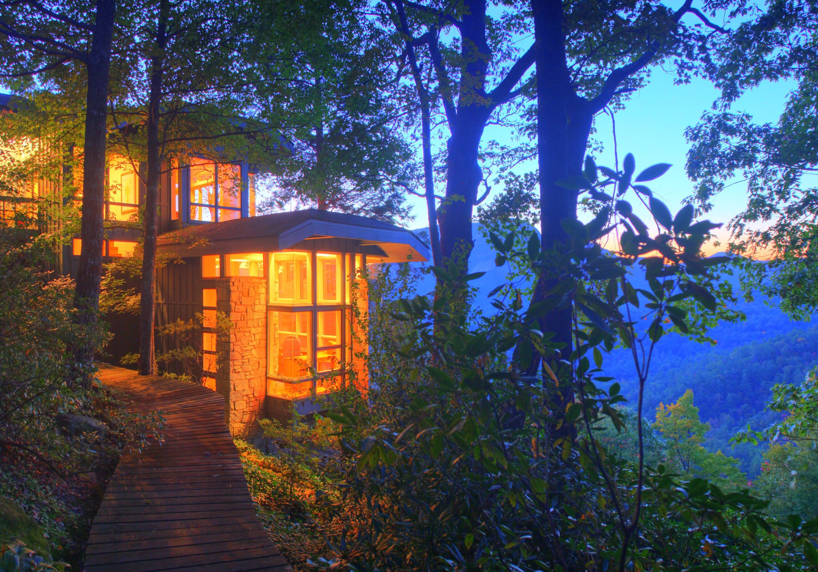 A cozy treehouse glowing warmly at dusk amidst lush greenery.